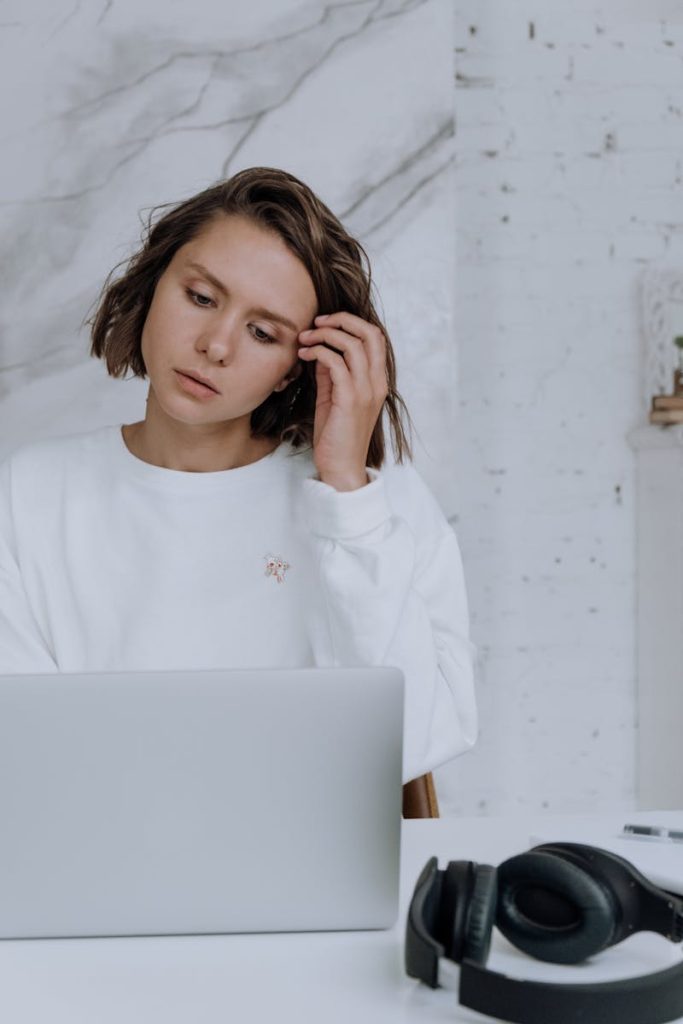 Young woman in modern Scandinavian interior working on laptop with headphones beside her.